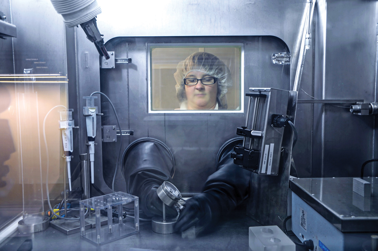 A researcher works with metal objects in a closed laboratory hood.